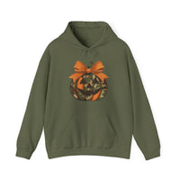 Jackie O Hoodie: Olive-green pullover with a kangaroo pocket and drawstring hood, featuring a stylized jack-o’-lantern graphic with orange and camouflage segments and a bow.