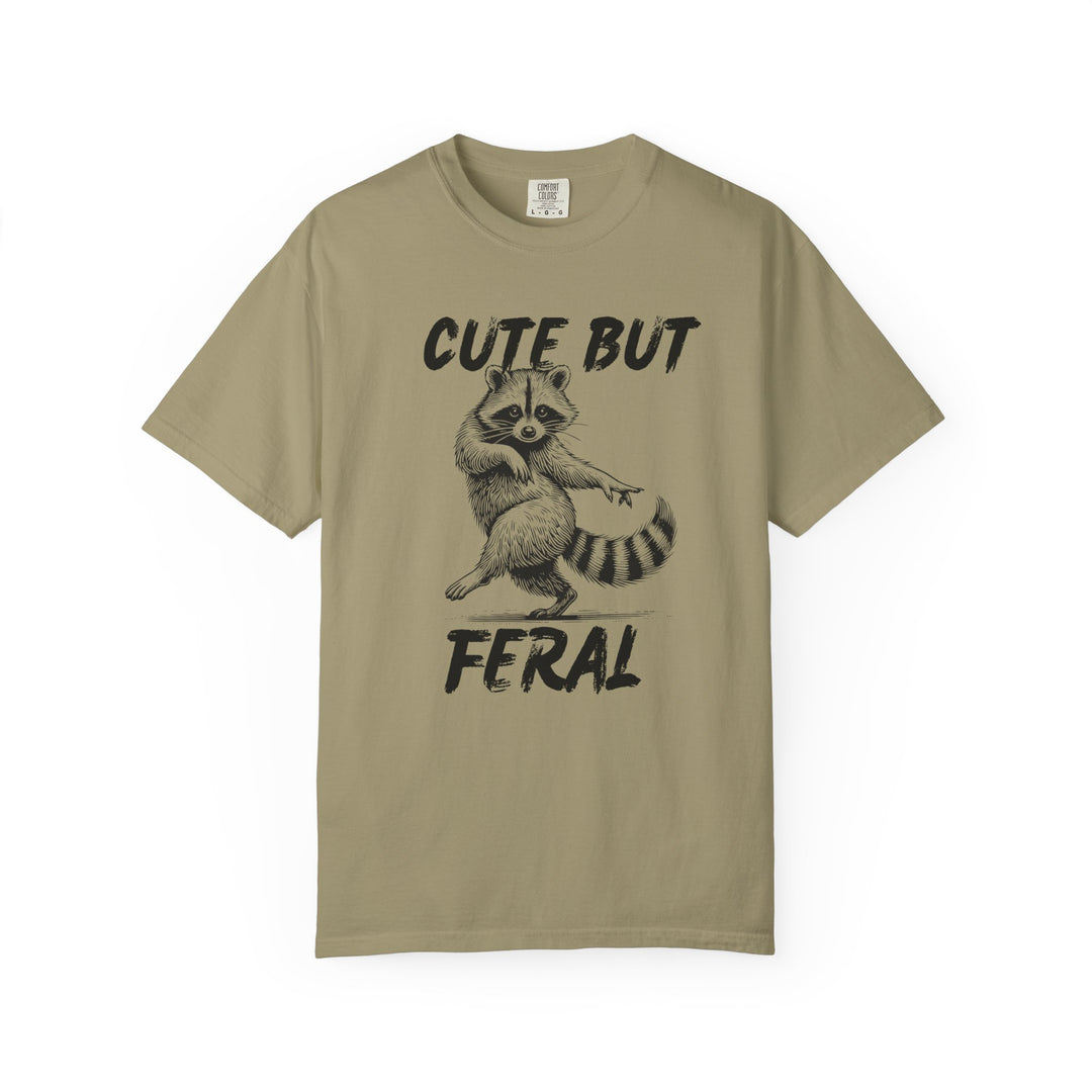 Cute but Feral Tee features a playful raccoon graphic and hand-brushed text on a cozy, khaki cotton shirt, ideal for casual, unique style.