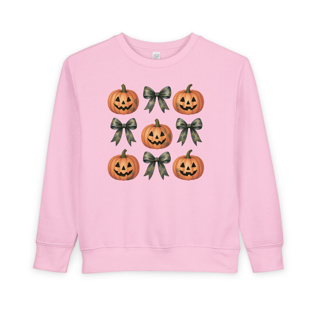 Light-pink toddler sweatshirt, Pumpkins and Bows Toddler Crew, features a 3x3 grid with jack-o’-lanterns and camouflage bows, designed for comfort and durability.
