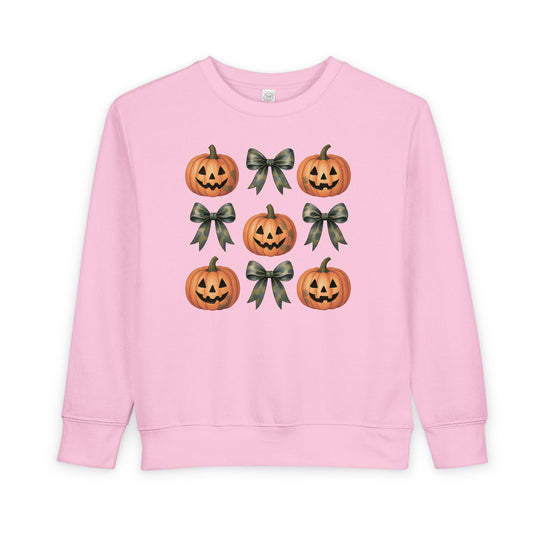 Light-pink toddler sweatshirt, Pumpkins and Bows Toddler Crew, features a 3x3 grid with jack-o’-lanterns and camouflage bows, designed for comfort and durability.