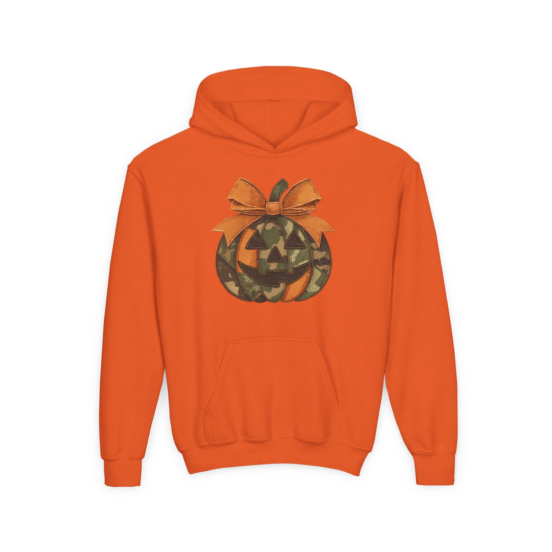 Jackie O Youth Hoodie features an orange pullover design with a camouflage jack-o’-lantern graphic and bow, offering a cozy, stylish fit with a kangaroo pocket.