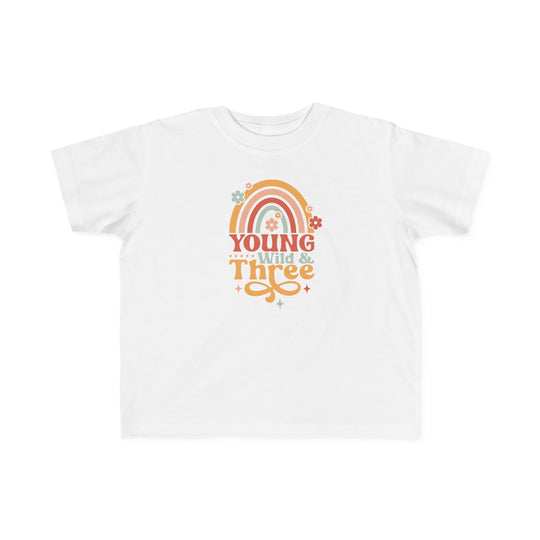 Young Wild and Three Toddler Tee featuring a white shirt with rainbow, flower, and text designs. Made of 100% combed ringspun cotton, light fabric, tear-away label, and a classic fit. Ideal for sensitive toddler skin.
