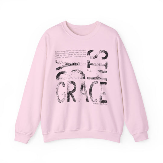 Pale-pink crew-neck sweatshirt with BY GRACE in black type and Romans 3:23–24 scripture quote, offering comfort and ethical, sustainable production.