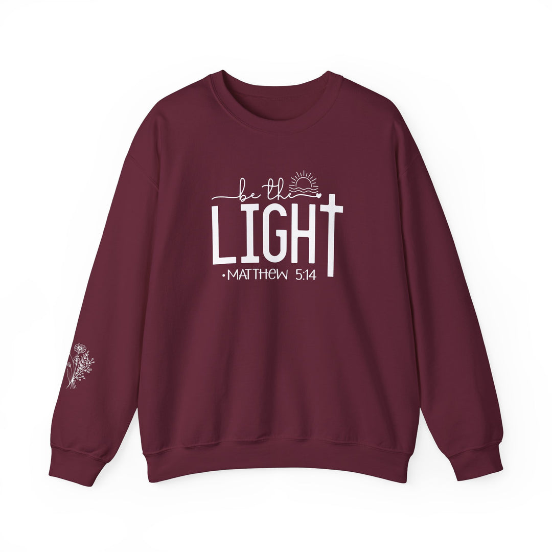 A maroon Be the Light Crew sweatshirt with white text, crafted from a cozy 50% cotton and 50% polyester blend. Ribbed knit collar, durable double-needle stitching, and tear-away label for itch-free comfort. Ideal for colder months.