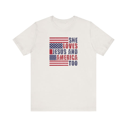 A beloved She Loves Jesus and America Tee, featuring red and blue text on a white shirt. Unisex jersey tee with ribbed knit collars, taping on shoulders, and tear away label. 100% Airlume combed cotton, retail fit, and light fabric.