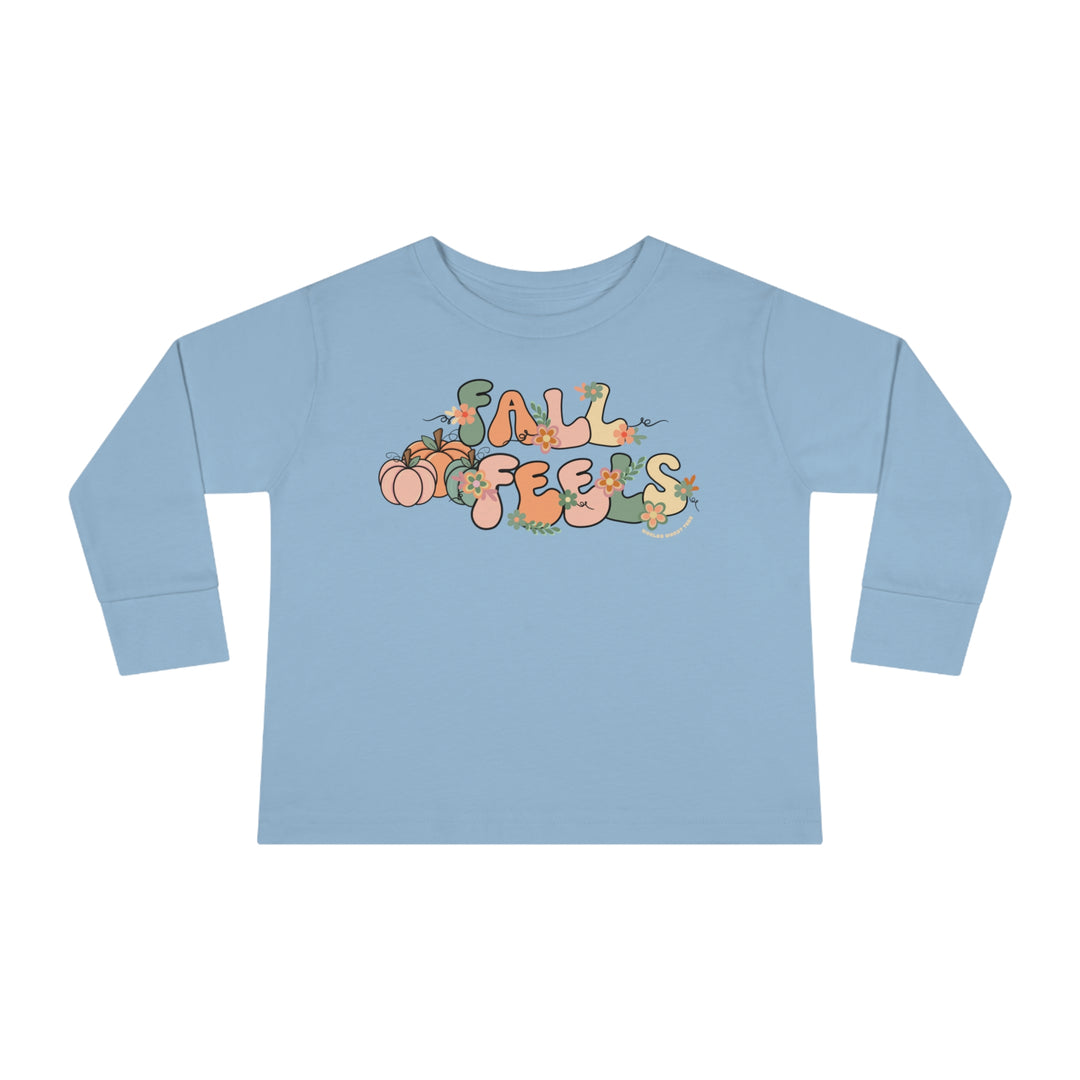 A custom Fall Feels Toddler Long Sleeve Tee in blue with playful designs of pumpkins, flowers, and letters. Made of 100% combed ringspun cotton, featuring a ribbed collar and EasyTear™ label for comfort and durability.