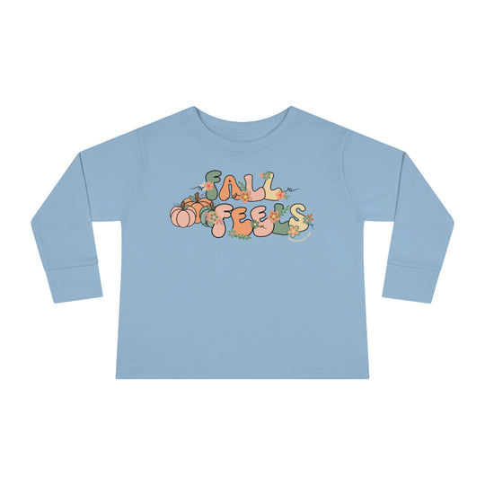 A custom Fall Feels Toddler Long Sleeve Tee in blue with playful designs of pumpkins, flowers, and letters. Made of 100% combed ringspun cotton, featuring a ribbed collar and EasyTear™ label for comfort and durability.