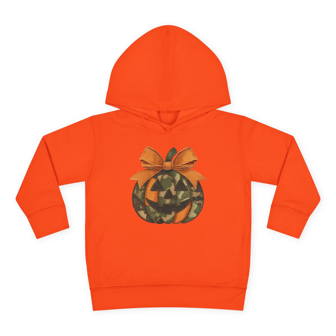 Jackie O Toddler Hoodie: Bright orange children’s hoodie with a jack-o’-lantern graphic featuring camouflage and solid orange segments, topped with a large bow.