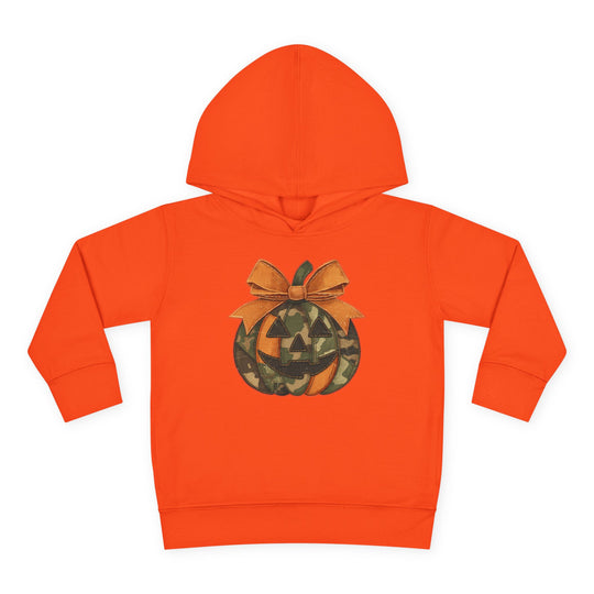 Jackie O Toddler Hoodie: Bright orange children’s hoodie with a jack-o’-lantern graphic featuring camouflage and solid orange segments, topped with a large bow.