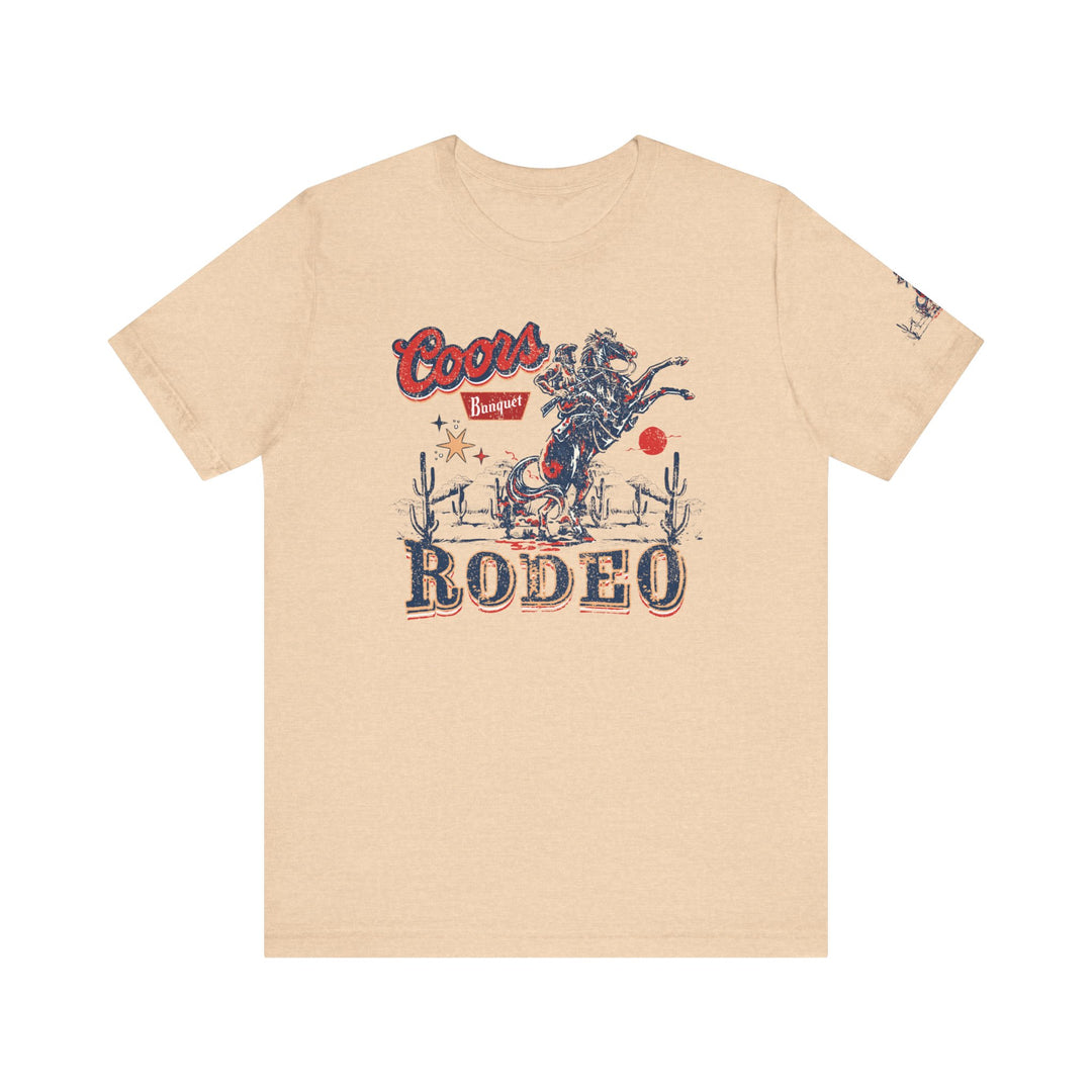 Coors Rodeo Tee: A tan t-shirt featuring a cowboy graphic. Unisex jersey tee with ribbed knit collar, 100% Airlume combed cotton, retail fit, tear away label. Sizes XS-3XL. Ideal for casual wear.