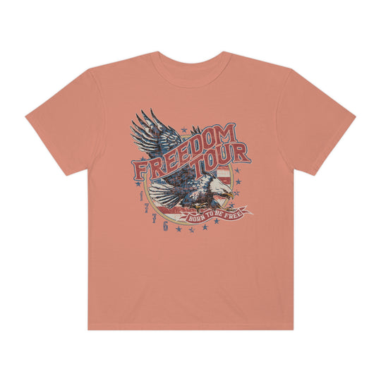 A Freedom Tour Tee, featuring an eagle graphic on a pink shirt. 100% ring-spun cotton, relaxed fit, double-needle stitching for durability, no side-seams for a tubular shape. Ideal for daily wear.