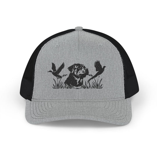 Bird Hunting Snapback Trucker Cap featuring a stamped dog silhouette amidst marsh grass with flying waterfowl, gray front, black mesh back, adjustable snap closure.