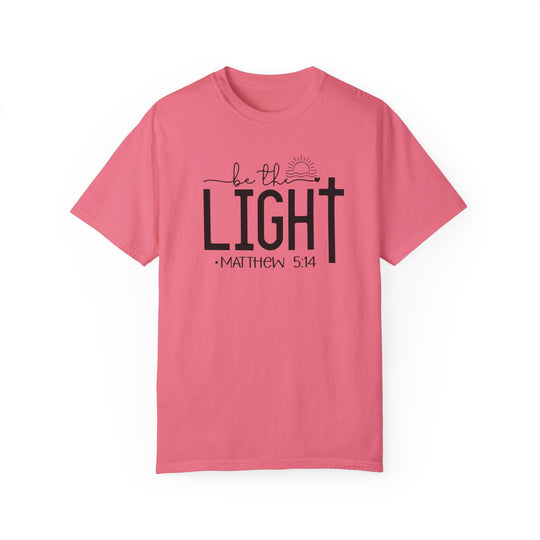 A ring-spun cotton Be the Light Tee in pink with black text. Garment-dyed for extra coziness, featuring a relaxed fit, double-needle stitching, and no side-seams for durability and shape retention.