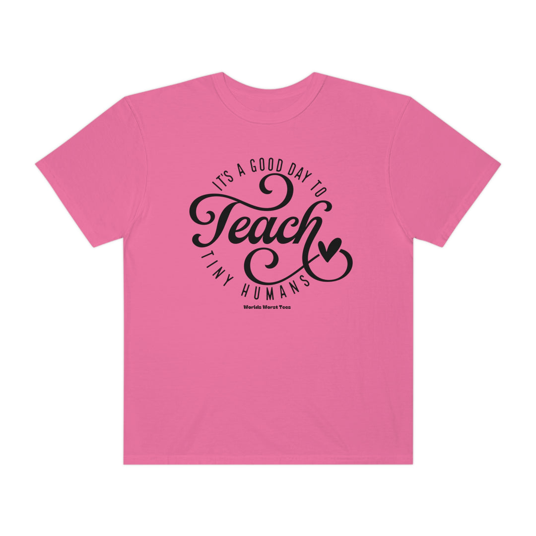 A Teach Tiny Humans Tee, a pink shirt with black text, in a relaxed fit, made of 80% ring-spun cotton and 20% polyester, featuring a rolled-forward shoulder and back neck patch.