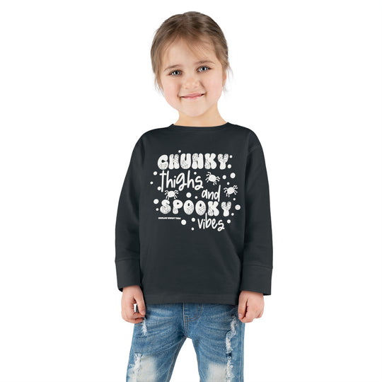 A toddler wearing a black long-sleeve tee with white text and spider design. Made of 100% combed ringspun cotton, featuring ribbed collar and EasyTear™ label for comfort and durability. From 'Worlds Worst Tees'.