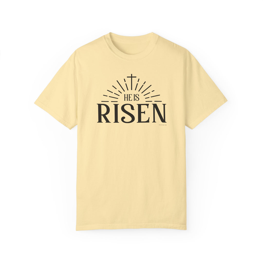 A ring-spun cotton He is Risen Tee in yellow with black text, featuring a cross and rays of light design. Garment-dyed for extra coziness, with a relaxed fit and durable double-needle stitching.