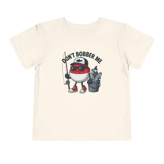 Cartoon fishing bobber character with sunglasses and cap on light T-shirt, holding rod and fish bucket. Slogan: DON’T BOBBER ME. Toddler sizes available.