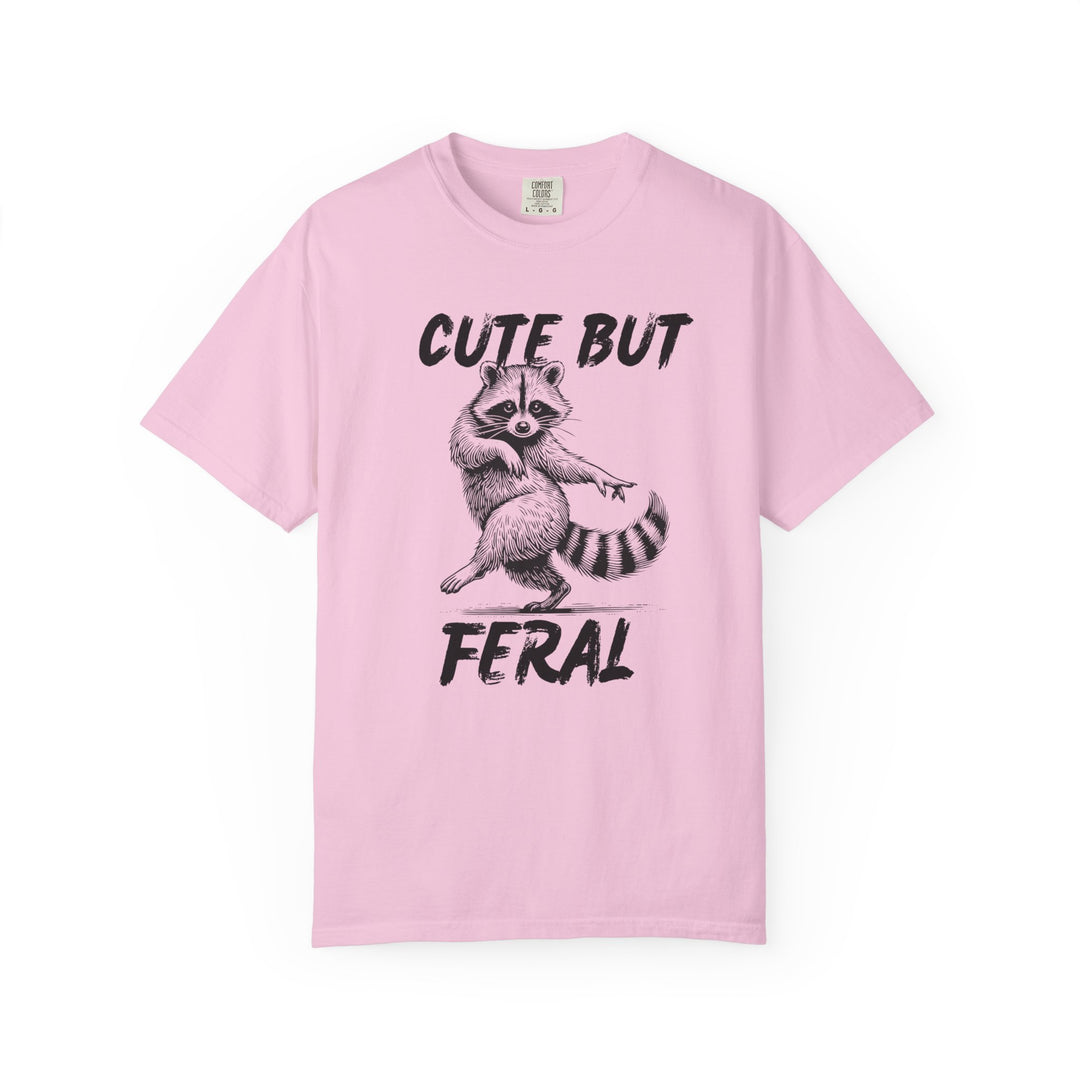 Light-pink Cute but Feral tee with playful raccoon illustration, emphasizing a humorous theme; relaxed fit, durable ring-spun cotton for comfort.