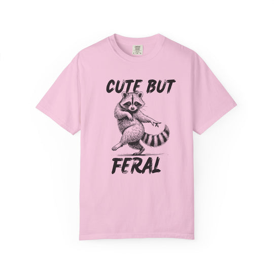 Light-pink Cute but Feral tee with playful raccoon illustration, emphasizing a humorous theme; relaxed fit, durable ring-spun cotton for comfort.