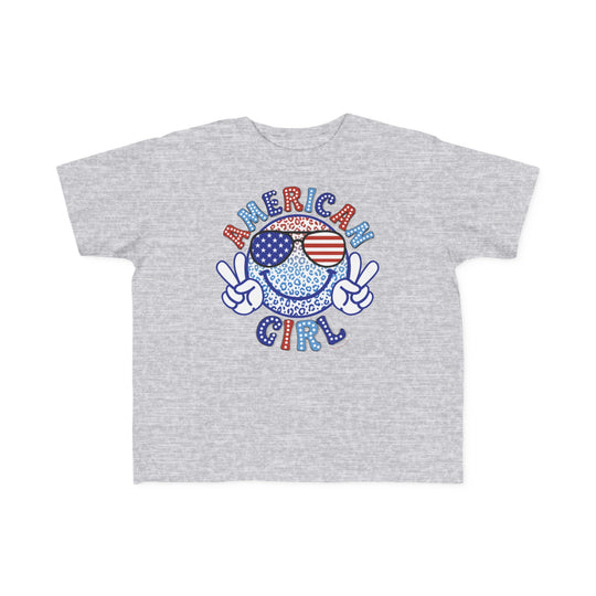 American Girl Toddler Tee featuring a cartoon character making a peace sign on a grey shirt. Soft 100% combed ringspun cotton, light fabric, tear-away label, classic fit. Available in sizes 2T to 5-6T.