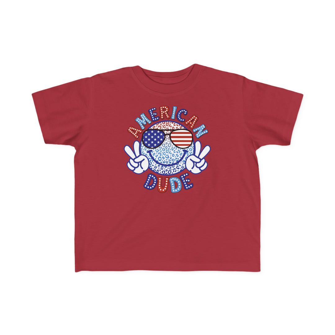 American Dude Toddler Tee featuring a red shirt with a cartoon character and logo. Soft 100% combed ringspun cotton, light fabric, tear-away label, classic fit. Sizes: 2T, 3T, 4T, 5-6T.