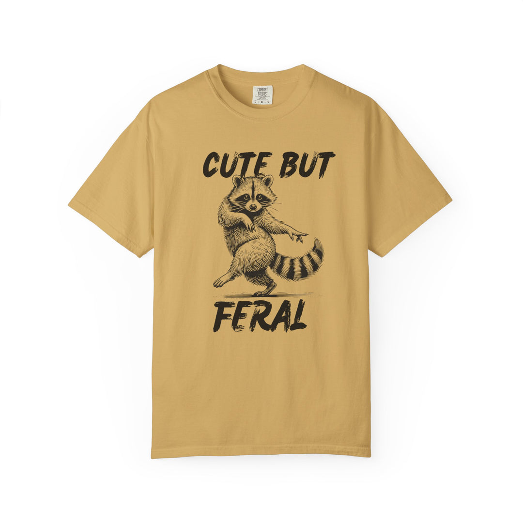 Cute but Feral Tee featuring a playful dancing raccoon illustration and slogan, designed on a mustard-yellow Comfort Colors short-sleeve T-shirt known for its comfort and durability.