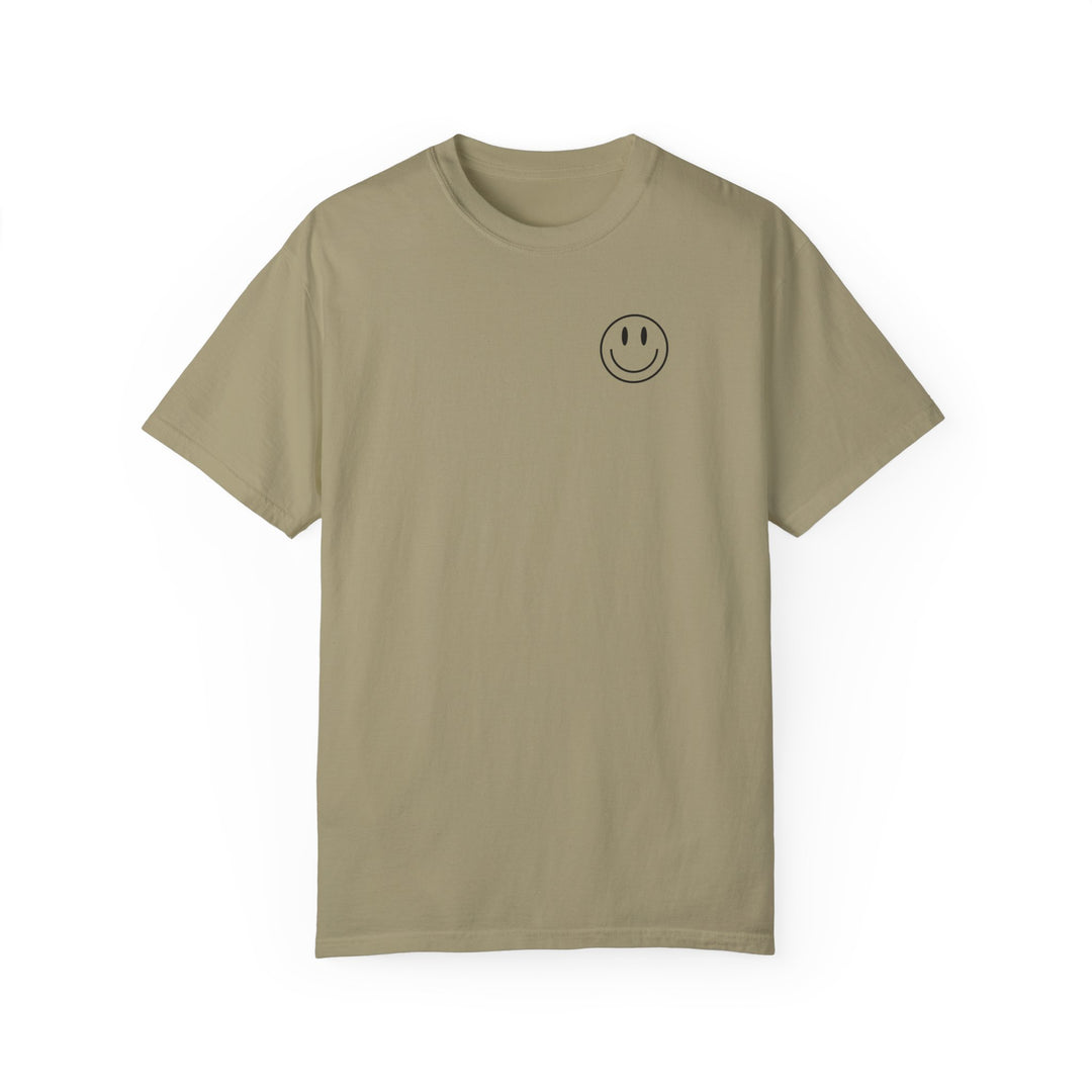 A tan t-shirt featuring a smiley face design, the God Day to Have a Good Day Tee from Worlds Worst Tees. Made of 100% ring-spun cotton, garment-dyed for softness, with a relaxed fit and durable double-needle stitching.