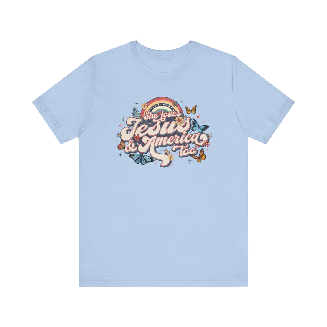 A light blue She Loves Jesus and America Tee, featuring butterflies and flowers graphic design. Unisex jersey tee made of 100% cotton, with ribbed knit collars and tear away label. Sizes XS to 3XL.