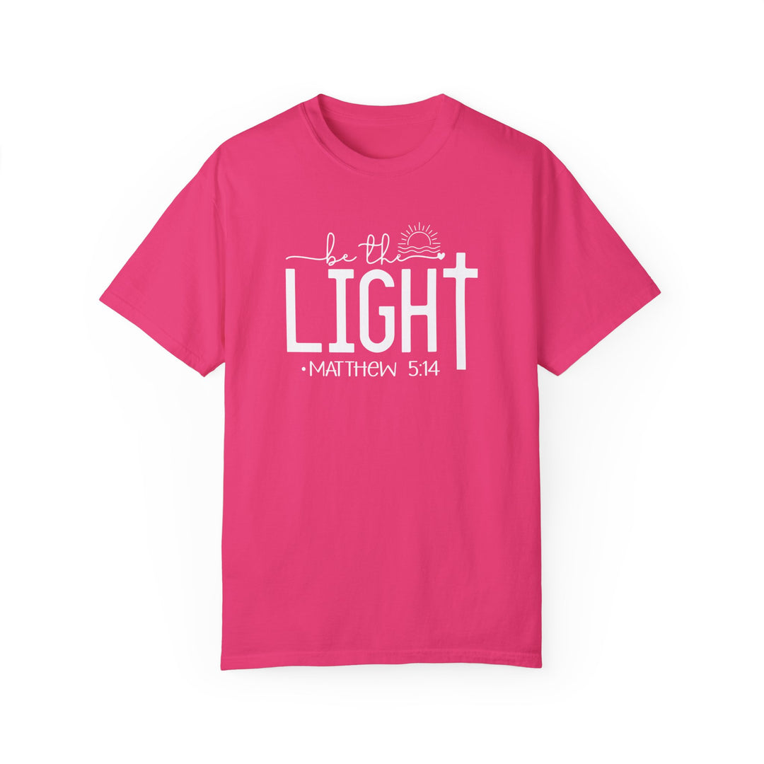 A ring-spun cotton Be the Light Tee in pink with white text. Garment-dyed for coziness, featuring a relaxed fit, double-needle stitching, and no side-seams for durability and shape retention.
