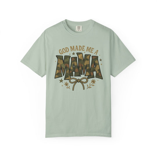 Light sage-green T-shirt with 'GOD MADE ME A MAMA' in camouflage and mustard, featuring a bow and doodles, from Comfort Colors.