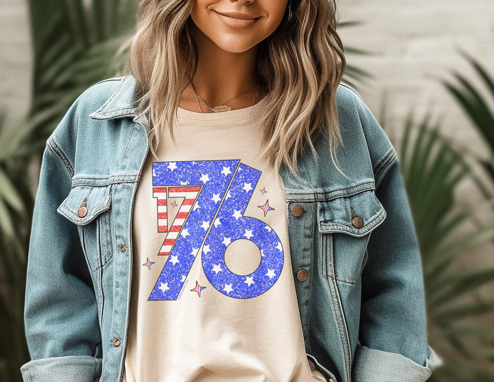 A woman in a denim jacket wearing sunglasses, showcasing the 1776 Tee. Unisex jersey tee with ribbed knit collar, taping on shoulders, and Airlume combed cotton. Reflects the store's unique graphic t-shirts.