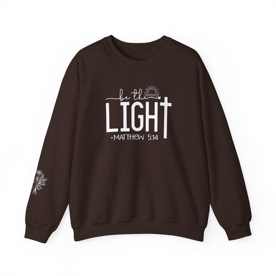 A cozy unisex heavy blend crewneck sweatshirt, the Be the Light Crew, in brown with white text. Made of 50% cotton and 50% polyester, featuring ribbed knit collar and double-needle stitching for durability.