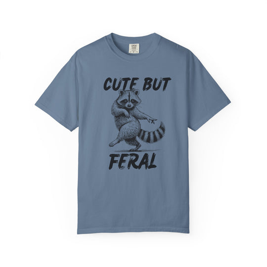 Slate-blue Comfort Colors Cute but Feral tee featuring a black illustration of a dancing raccoon, with bold text above and below, ideal for casual wear.