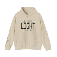 A beige unisex heavy blend hooded sweatshirt with black text, featuring a kangaroo pocket and matching drawstring. Made of 50% cotton and 50% polyester, this cozy and stylish Be the Light Hoodie is perfect for chilly days.