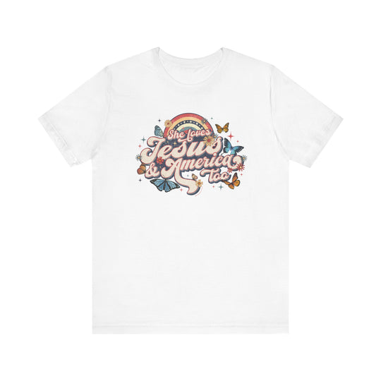 A white t-shirt featuring a graphic design of butterflies, flowers, and colorful text. Unisex jersey tee made of 100% Airlume combed cotton, with ribbed knit collars and tear-away label. She Loves Jesus and America Tee from Worlds Worst Tees.