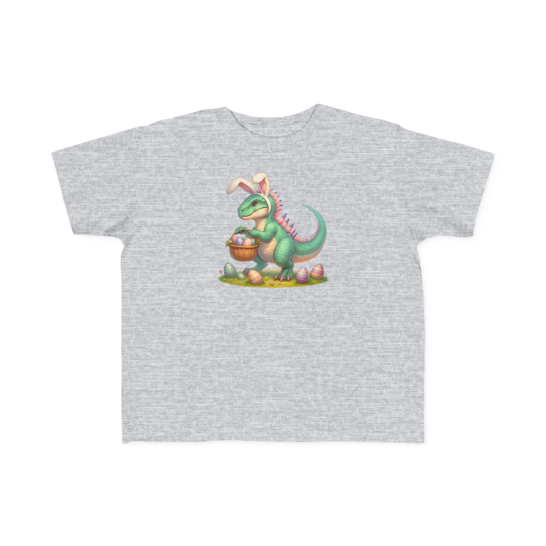 A soft, durable Eggosaurus Toddler Tee featuring a cartoon dinosaur with a basket of eggs. Made of 100% combed ringspun cotton, light fabric, and a tear-away label. Ideal for sensitive skin and playtime adventures.
