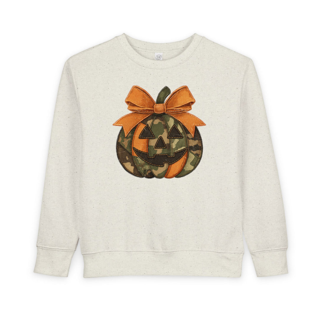 Jackie O Toddler Crew: Cream crewneck sweatshirt with a stylized jack-o’-lantern graphic, featuring orange and camouflage segments, and a large orange bow.