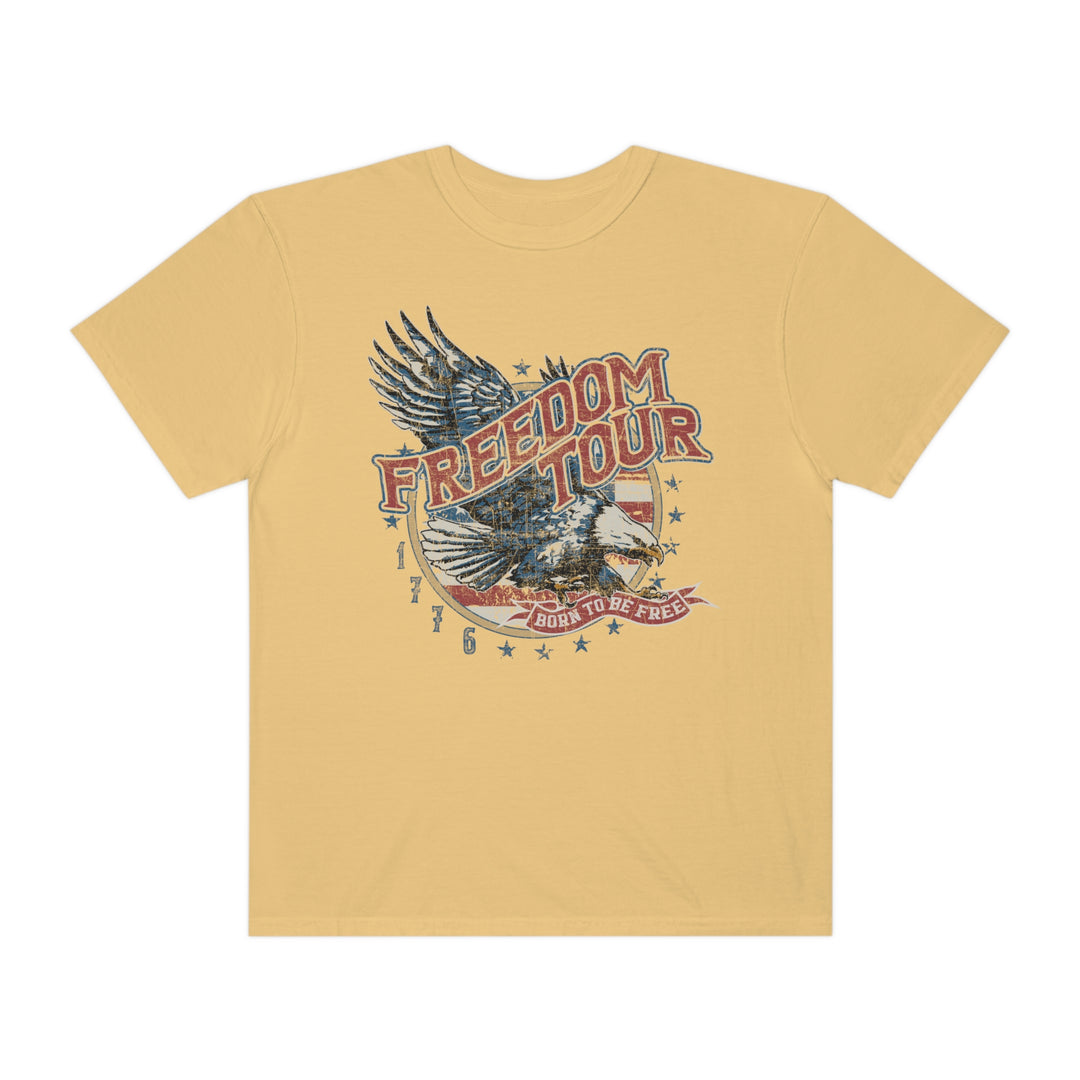 Freedom Tour Tee: A yellow t-shirt with a graphic eagle design. 100% ring-spun cotton, garment-dyed for extra coziness. Relaxed fit, double-needle stitching for durability, no side-seams for a tubular shape.
