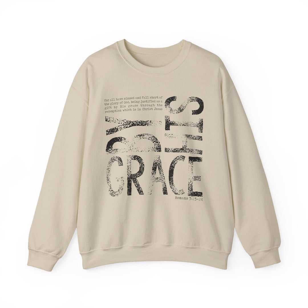Cream-colored sweatshirt with BY GRACE in bold letters and Romans 3:23–24 verse, offering comfort and style with a durable, ethically made fabric blend.