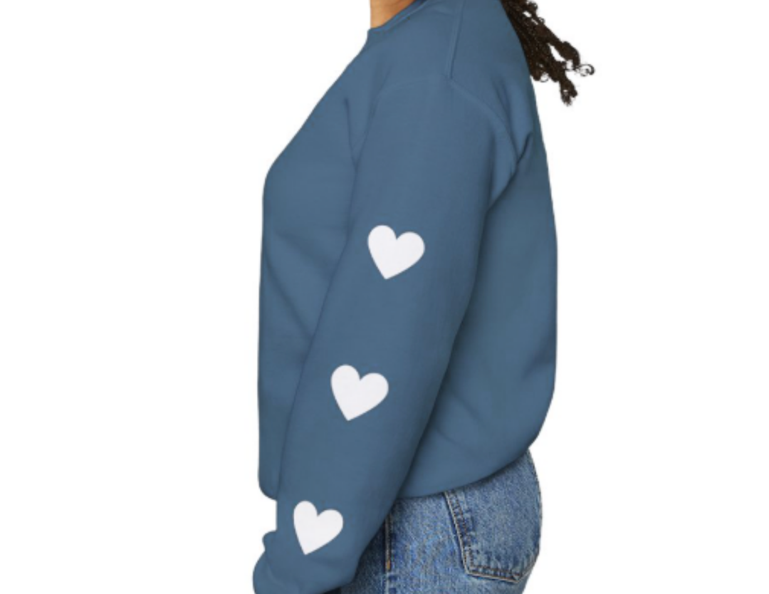 Side profile of a person in a blue Footprints of Kindness Crew sweatshirt with white heart graphics on sleeves, paired with medium-wash jeans.