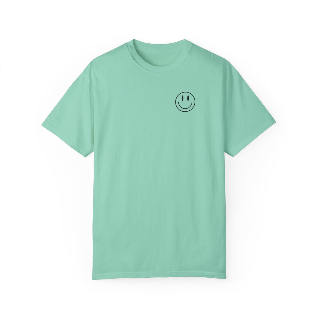 A relaxed-fit God Day to Have a Good Day Tee, featuring a smiley face on a green shirt. 100% ring-spun cotton, garment-dyed for extra coziness. Double-needle stitching for durability, no side-seams for a tubular shape.