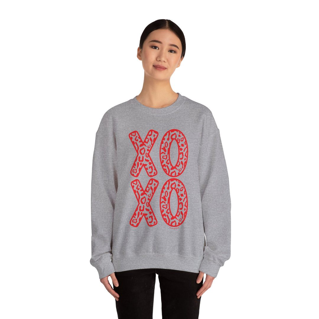 A unisex heavy blend crewneck sweatshirt featuring red XOXO text on grey fabric. Made of 50% cotton and 50% polyester, with ribbed knit collar for shape retention. Comfortable and versatile.