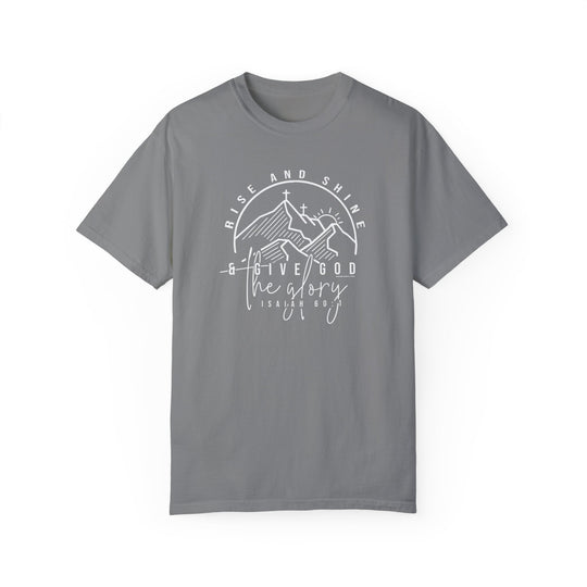 A grey Rise and Shine Tee, featuring white text, a cross, and mountains. 100% ring-spun cotton, garment-dyed for coziness. Relaxed fit with durable double-needle stitching and no side-seams for a tubular shape.