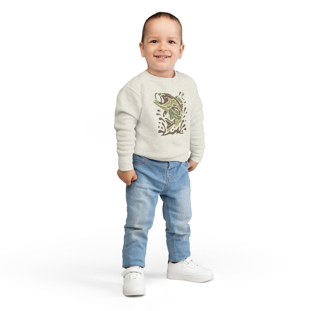 Toddler in a cream Camo Fish Toddler Crew sweatshirt, light-blue jeans, and white sneakers, smiling against a white background.