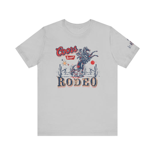 A classic Coors Rodeo Tee featuring a graphic cowboy design on a white shirt. Unisex jersey tee with ribbed knit collars, taping on shoulders, and 100% Airlume combed cotton. Retail fit, tear away label, and true-to-size fit.