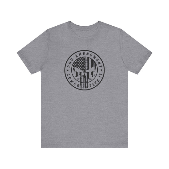 A grey t-shirt featuring a graphic design with a skull, flag, and logo. Unisex jersey tee made of 100% Airlume combed cotton, retail fit, tear-away label, and ribbed knit collars for comfort. Product title: 2nd Amendment Come and Take It Tee.