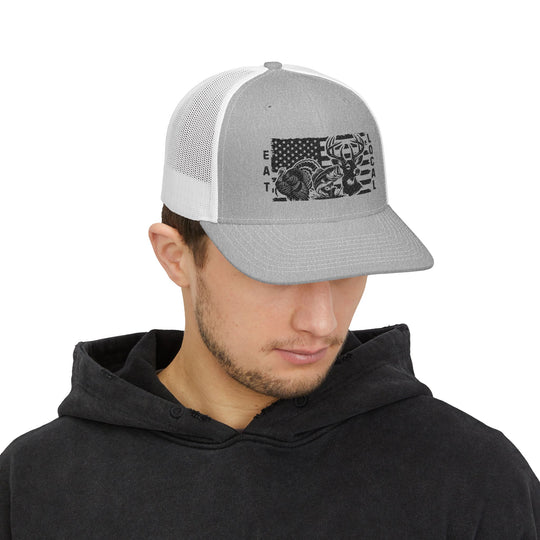 Young man models the Eat Local Snapback Trucker Cap featuring wildlife silhouettes and American flag graphic, paired with a dark hoodie.