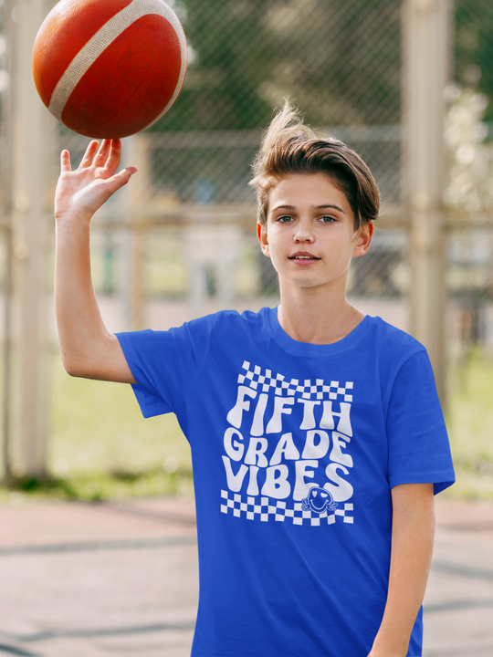 A boy in a blue shirt holding a basketball, embodying 5th Grade Vibes Tee. Kids heavy cotton tee, 100% cotton, tear-away label, classic fit, ideal for everyday wear.