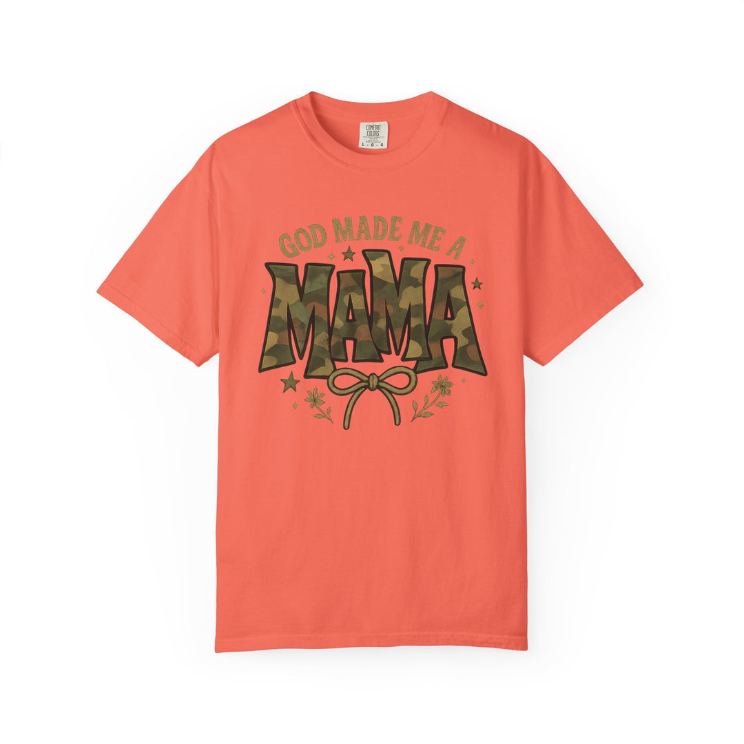 Coral short-sleeve tee, “God Made Me a Mama,” with camouflage MAMA graphic, bow, floral, and star accents. Cozy, durable, relaxed fit.
