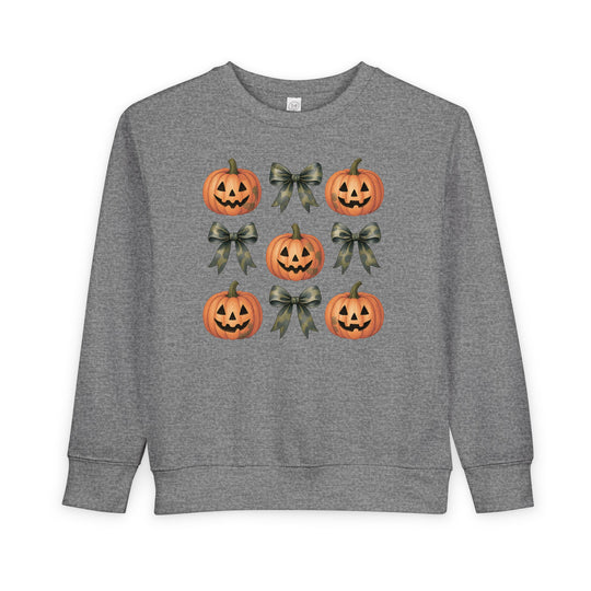 Pumpkins and Bows Toddler Crew: A heather-gray sweatshirt featuring a 3x3 grid of smiling jack-o-lanterns and camouflage-patterned ribbon bows, designed for comfort and style.